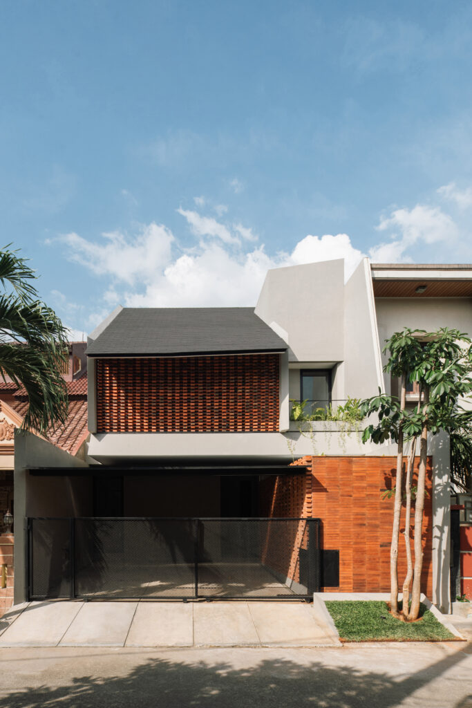 DDD Residence in Karawaci – A stunning collaboration with architect Dhaniesal, featuring a contemporary design that combines sleek modern architecture with natural elements. The façade showcases a beautiful blend of textured brickwork and minimalist white walls, framed by lush greenery and a geometric fence, creating a welcoming yet stylish residential space.