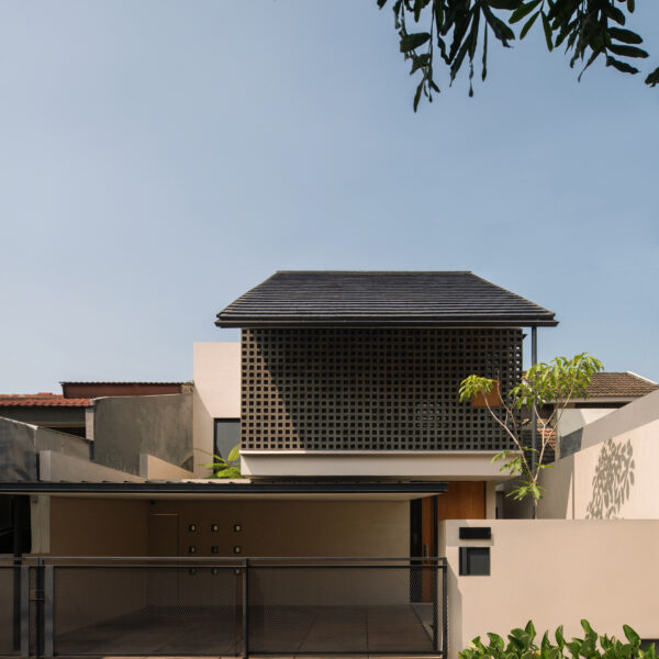 Front view of A&T Residence, a two-story modern tropical house with a clean beige façade, gable roof, and prominent upper-level square concrete vent block screen, constructed by NDA in collaboration with architect Dhaniesal.